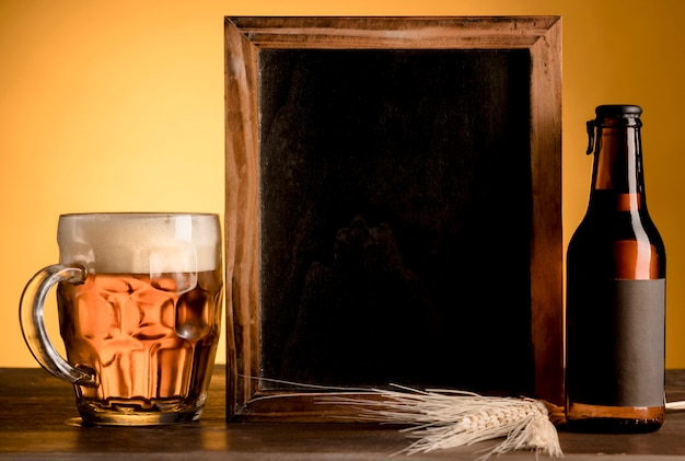 Pizarra y vaso de cerveza y botella alcohólica en mesa de madera