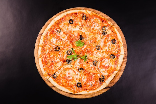 Pizza con aceitunas y tomates en una tabla de madera sobre un fondo negro