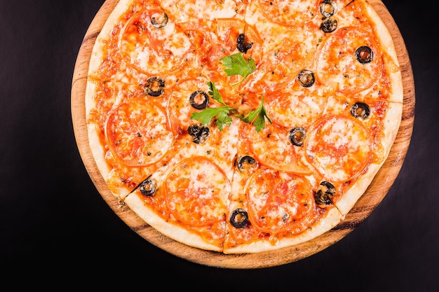 Pizza con aceitunas y tomates en una tabla de madera sobre un fondo negro