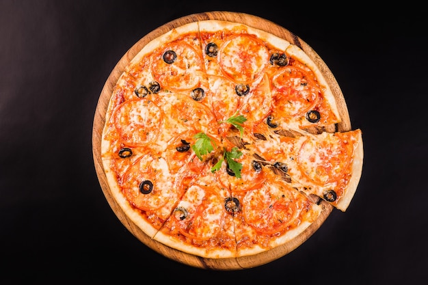 Pizza con aceitunas y tomates en una tabla de madera sobre un fondo negro