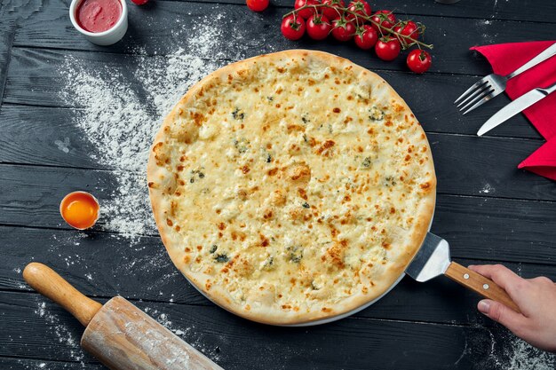 Pizza al horno con 4 tipos de queso, salsa blanca y sobre una mesa de madera negra en una composición con ingredientes. Vista superior