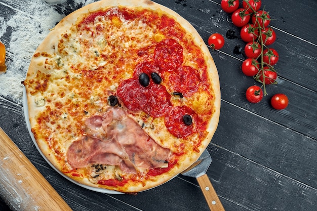 Pizza al horno con salami, jamón y pollo con salsa roja y queso derretido sobre una mesa de madera negra en una composición con ingredientes. Vista superior