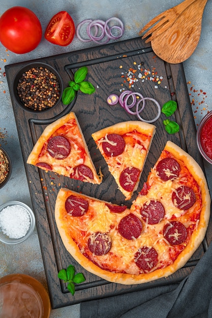 Pizza con albahaca, queso y salami sobre una tabla para cortar sobre un fondo gris. Concepto de comida rápida. Vista vertical.