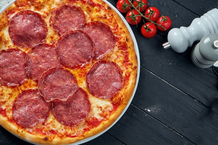 Foto pizza assada com chouriço de salame com molho vermelho e queijo derretido em uma mesa de madeira preta em uma composição com ingredientes. vista do topo