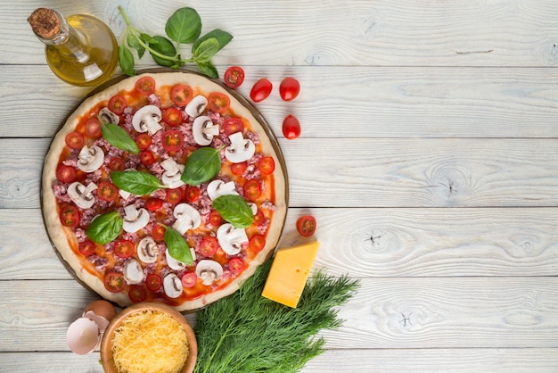 Pizza auf dem Stein zum Backen von Pizza und Zutaten der Pizza auf einer hölzernen Hintergrundoberansicht