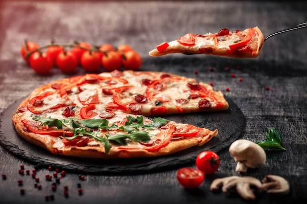 Pizza auf einem Spatel mit geräucherten Würstchen, Käse, Champignons, Kirschtomaten, Paprika auf einem Stein.