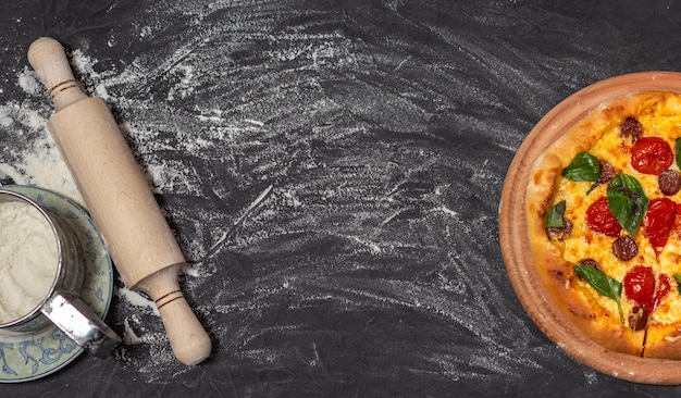 Pizza auf Holzplatte auf schwarzem Stein Hintergrund Nudelholz und Boden Käsepizza mit Tomate