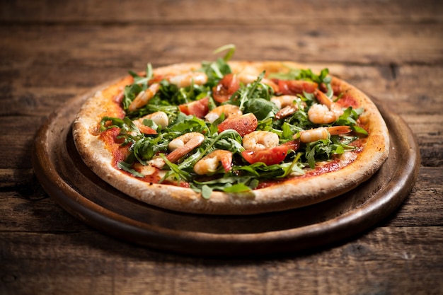 Pizza bedeckt mit Roquette und Garnelen auf Holztisch hautnah