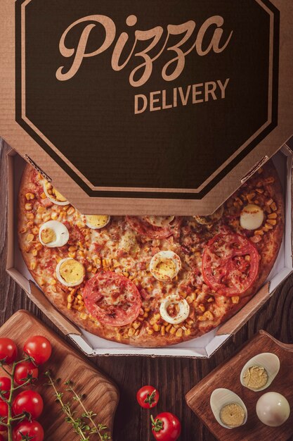 Foto pizza brasileira com mussarela, milho, bacon, ovos, tomate e orégano em caixa delivery (pizza especial) - vista de cima.