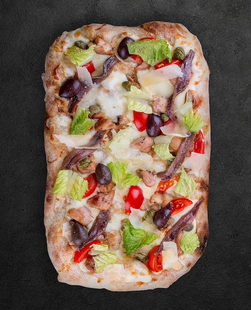 Pizza Caesar com anchovas de frango romaine cherry kalamata alcaparras pesto Pizza romana retangular em fundo escuro