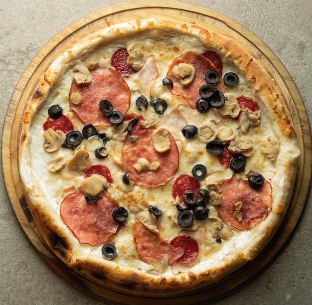 Pizza caliente italiana lista con aceitunas, queso y salchichas en un primer plano de fondo gris. Vista desde arriba.
