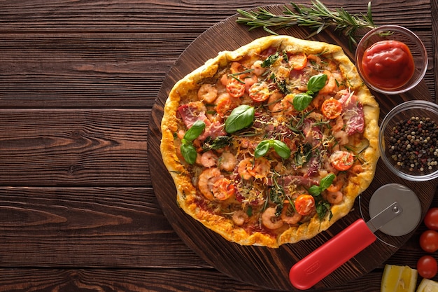 Pizza con camarones, tomates, queso y hierbas sobre un fondo de madera