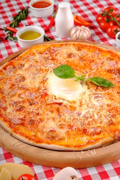 Foto pizza carbonara com bacon, ovo, queijo parmesão, manjericão fresco e molho de tomate em uma placa de madeira