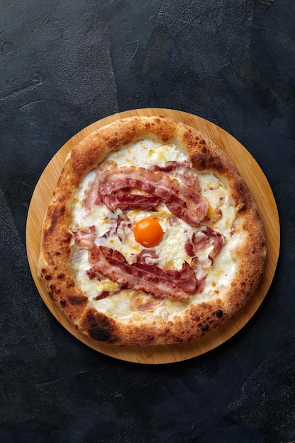 Pizza Carbonara sobre fondo de piedra negra. Pizza italiana Carbonara con tocino, huevo y queso, copie el espacio.