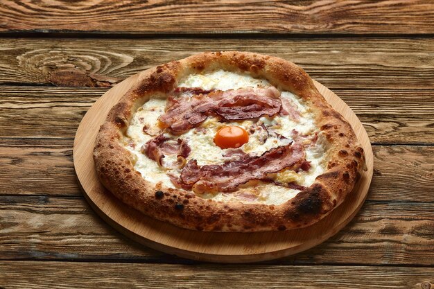 Pizza carbonara con tocino y huevo sobre fondo de madera