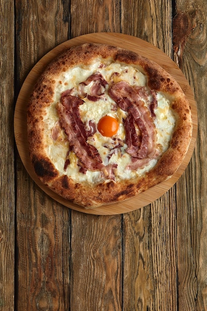 Pizza carbonara con tocino y huevo sobre fondo de madera