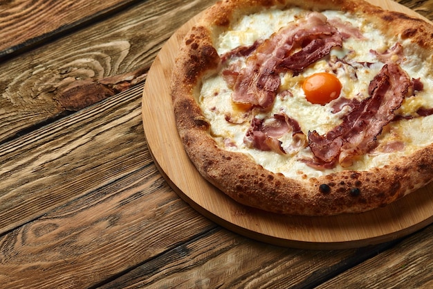 Pizza carbonara con tocino y huevo sobre fondo de madera