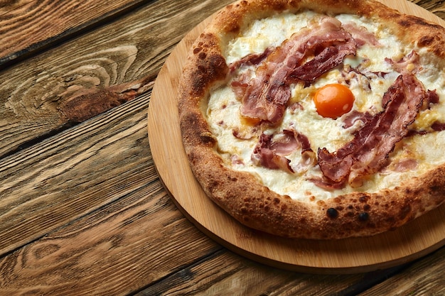 Pizza carbonara con tocino y huevo sobre fondo de madera