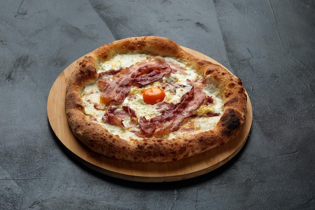 Pizza carbonara con tocino y huevo sobre fondo de piedra oscura