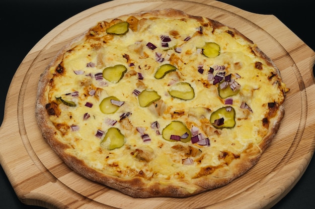 Pizza de carne italiana con tocino, cebolla y pepinos encurtidos sobre tabla de madera sobre fondo negro