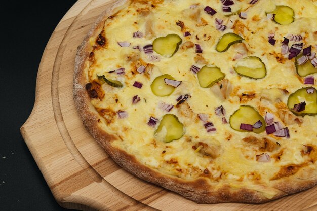 Pizza de carne italiana con tocino, cebolla y pepinos encurtidos sobre tabla de madera sobre fondo negro