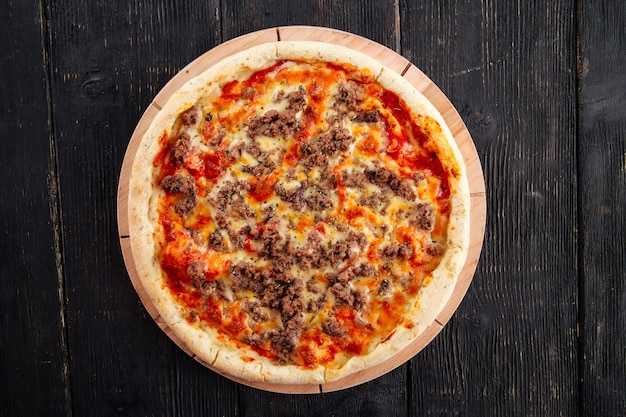 Pizza con carne picada y salsa de tomate en la mesa de madera oscura.