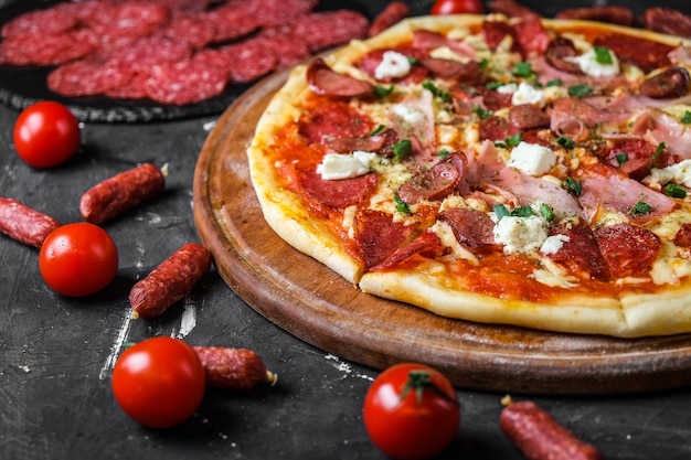 Pizza de carne con salami, jamón, pollo, salchichas y queso feta, en una pizarra y sobre una superficie oscura