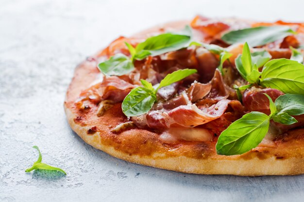 Pizza caseira com folhas de jamon, mussarela e manjericão fresco em um fundo claro de concreto. foco seletivo.