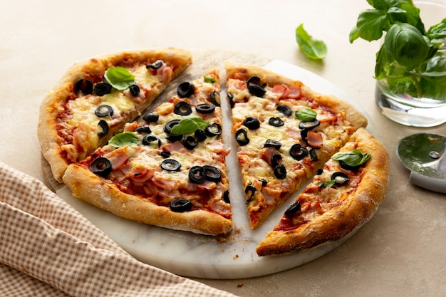 Pizza caseira com presunto, azeitonas pretas, queijo e manjericão fresco em prato de mármore