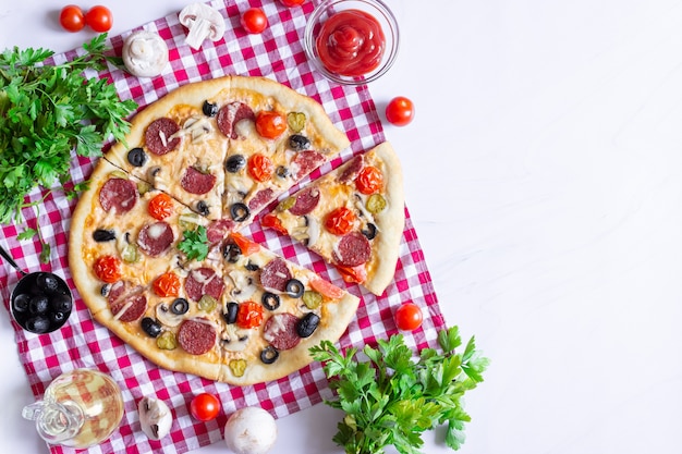Pizza caseira com salame, cogumelos e tomate cereja em um fundo branco. Uma toalha xadrez vermelha. Espaço livre para texto, vista superior.