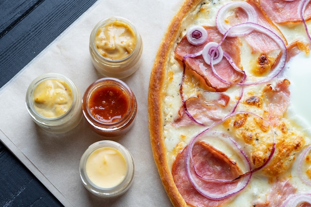 Pizza caseira deliciosa com ingridients na vista superior do fundo escuro. pizza plana leiga com salame, ovo, cebola e queijo derretido. viw de cima da cozinha italiana tradicional. comida para o almoço