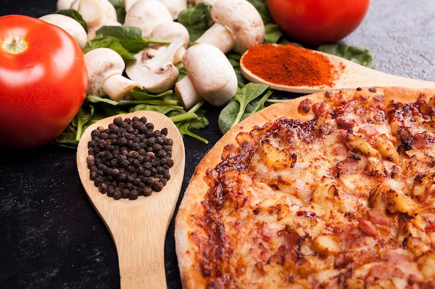 Foto pizza caseira recém-assada ao lado de cogumelos e tomates na mesa de madeira escura