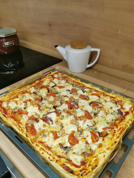 Pizza casera grande en una bandeja para hornear cuadrada con tomates queso ketchup cebollas ajo