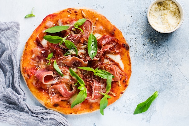 Pizza casera con jamón, mozzarella y hojas de albahaca fresca sobre un viejo hormigón ligero