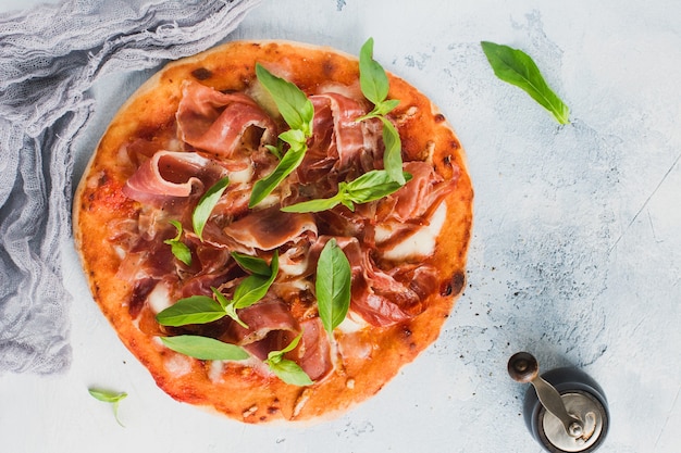 Pizza casera con jamón, mozzarella y hojas de albahaca fresca