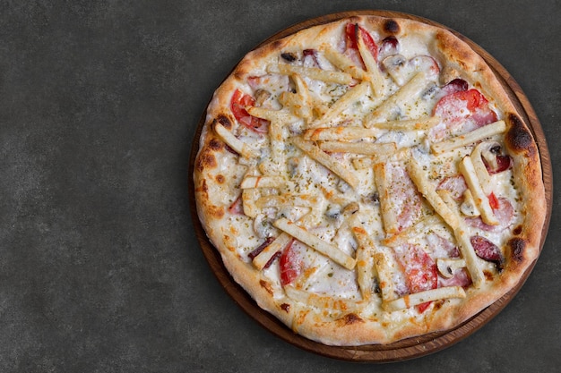 Pizza casera con salchichas, patatas, champiñones y tomates en una tabla redonda de madera