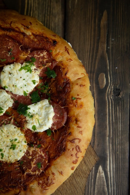Foto pizza casera sobre un fondo de madera oscura con tomate y salchicha en el tablero
