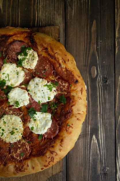 Foto pizza casera sobre un fondo de madera oscura con tomate y salchicha en el tablero