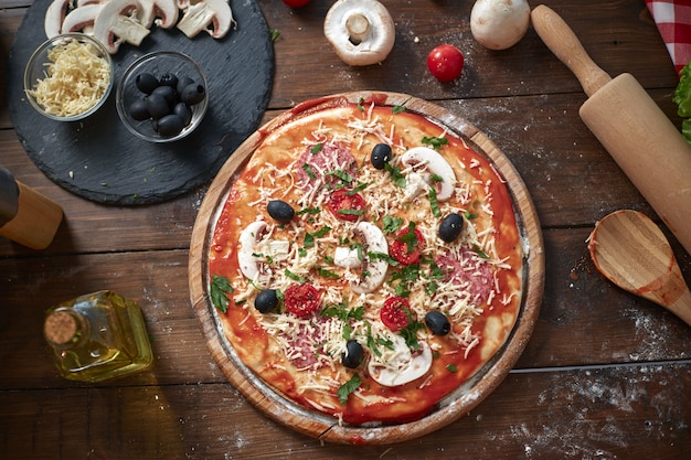 Pizza casera sobre tabla de madera, con tomates y salami, champiñones, estilo italiano en la mesa de madera vieja, vista superior