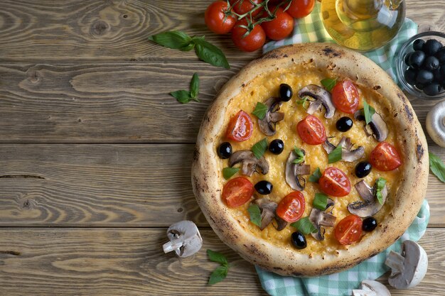 Pizza con champiñones, tomates y aceitunas sobre un fondo de madera