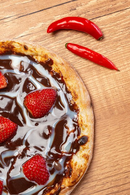 Pizza de chocolate con salsa de fresa y crema agria y pimientos rojos servidos en una mesa de madera