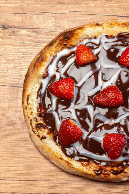 Pizza de chocolate con salsa de fresa y crema agria servida en una vista superior de la mesa de madera.