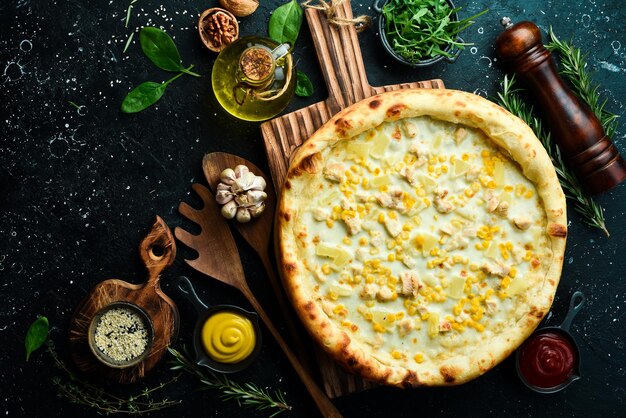 Pizza clássica com frango, abacaxi e queijo Pizza de queijo sobre um fundo de pedra preta Vista superior