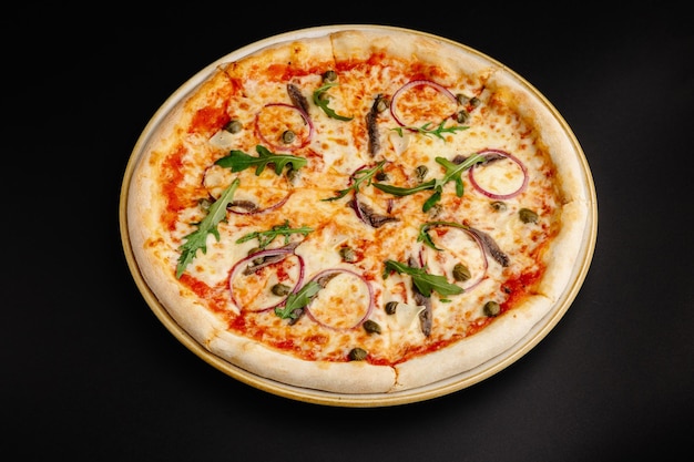 Foto pizza com anchoas, cebolas vermelhas, alcaparras e rúcula sobre um fundo preto