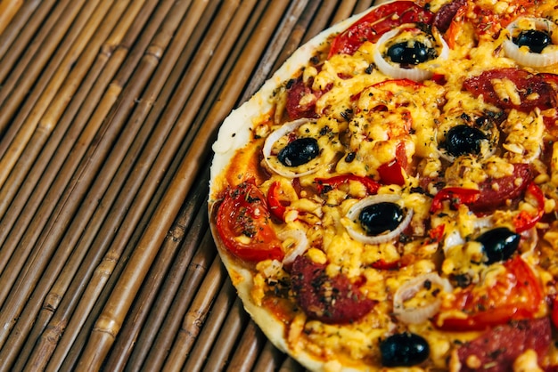 Pizza com azeitonas e salame em fundo de bambu