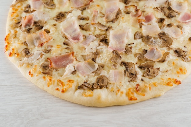 Pizza com bacon, cogumelos e queijo isolado em uma superfície de madeira branca