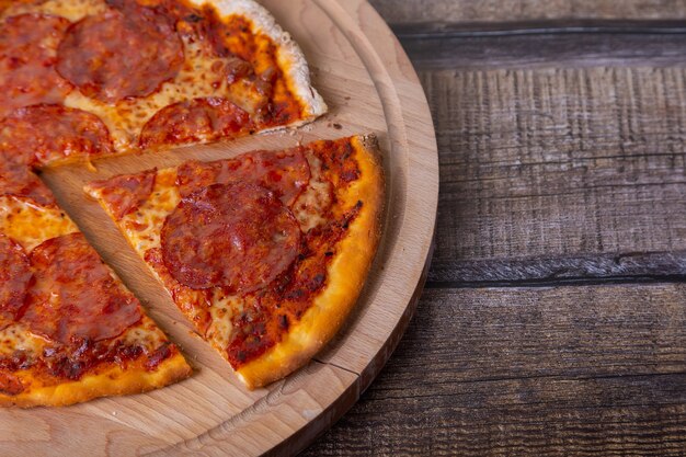 Pizza com chouriço em uma placa de madeira. Pizza inteira, uma peça cortada.