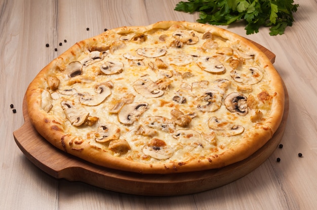 Pizza com frango e cogumelos em uma tábua de madeira