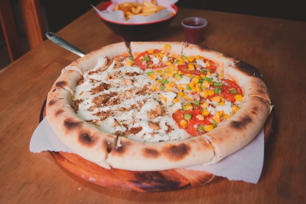 Pizza com legumes frango em pedaços pequenos e muito queijo em uma mesa de madeira