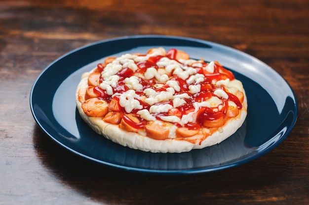 Pizza com linguiça e palitos de caranguejo em um prato de cerâmica azul sobre uma mesa de madeira